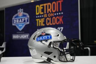 Ein Helm mit dem Logo des NFL-Drafts vor einer Werbewand mit dem Schriftzug "Detroit is on the Clock"